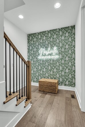 A staircase with wooden steps and black balusters, a woven basket, and a wall with a green floral pattern and a neon sign. - Luxe Downtown Home • Rooftop • Fireplace • DT ~2m (Nashville)