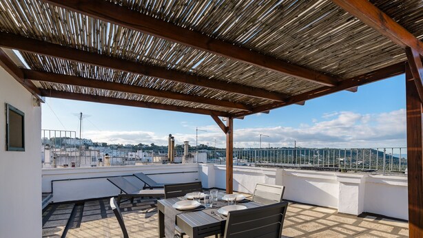 A rooftop terrace with a wooden pergola, a table set for dining, and a view of the cityscape.