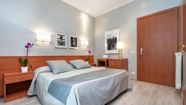 Un dormitorio moderno con una cama grande, mesitas de noche, un armario de madera y luces fijadas a la pared.