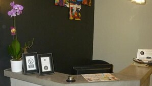 Un mostrador de recepción de diseño moderno, con una pared negra que presenta arte abstracto colorido, una orquídea en maceta y dos certificados enmarcados.