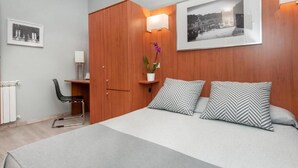 Un dormitorio moderno con cama, escritorio y silla. Hay un cuadro en la pared y una planta en maceta sobre el escritorio.