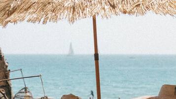 Una mesa en la playa con un paraguas de paja, sillas de mimbre y un letrero que dice 'NOÉ'.