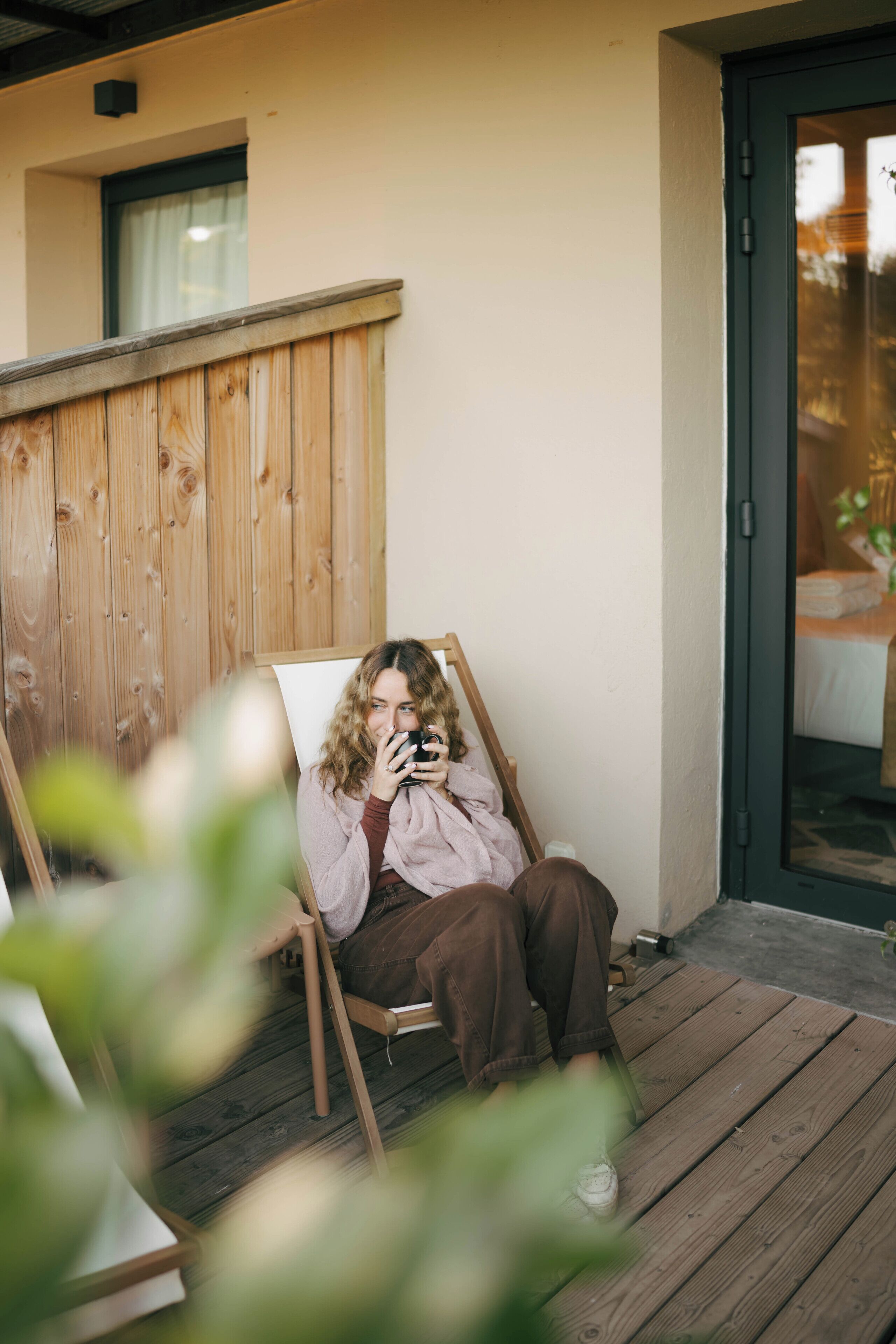 A person sitting on a wooden deck chair, holding a camera, with a wooden fence and a door in the background.