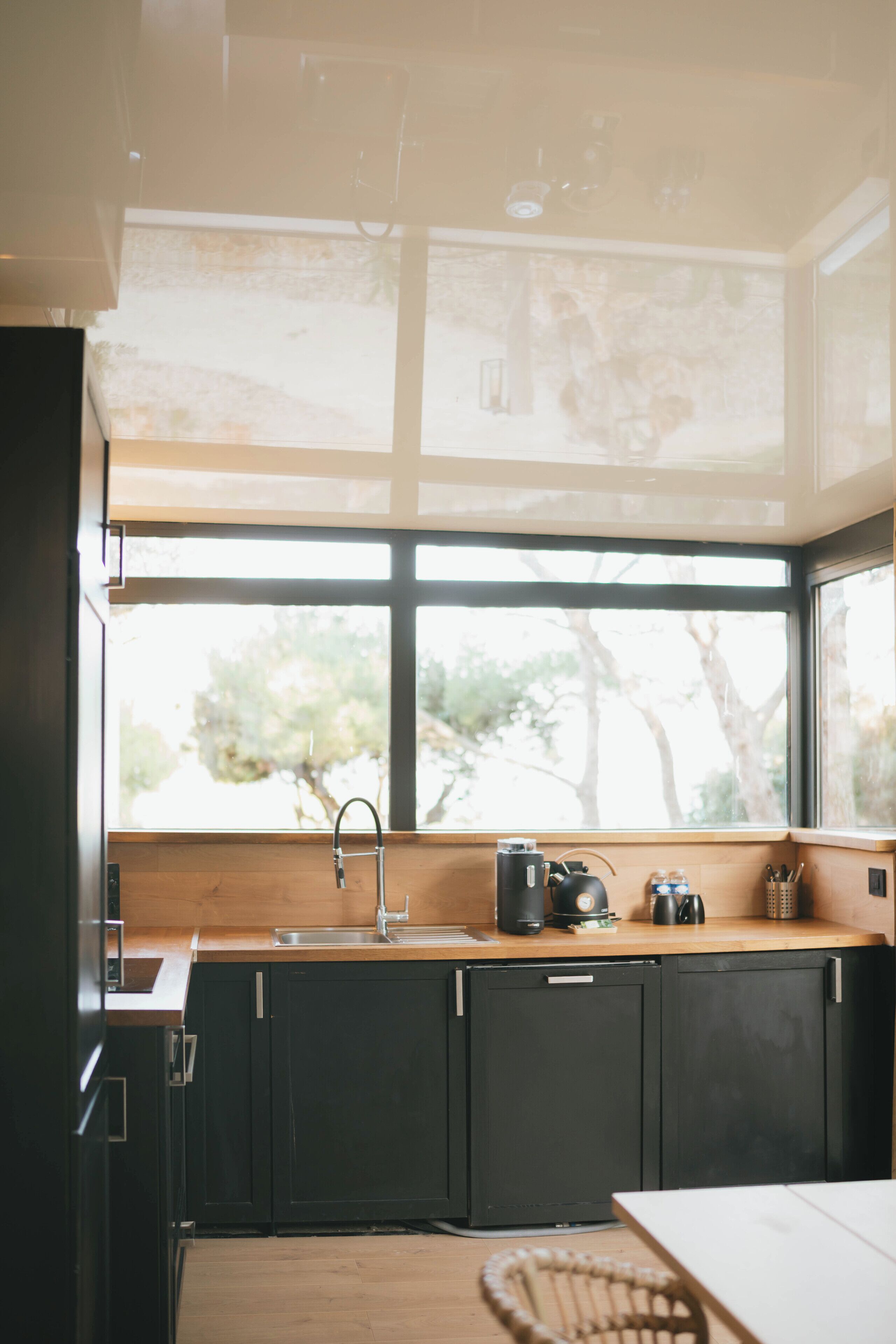 A modern kitchen with a large window, dark cabinets, and a wooden countertop.
