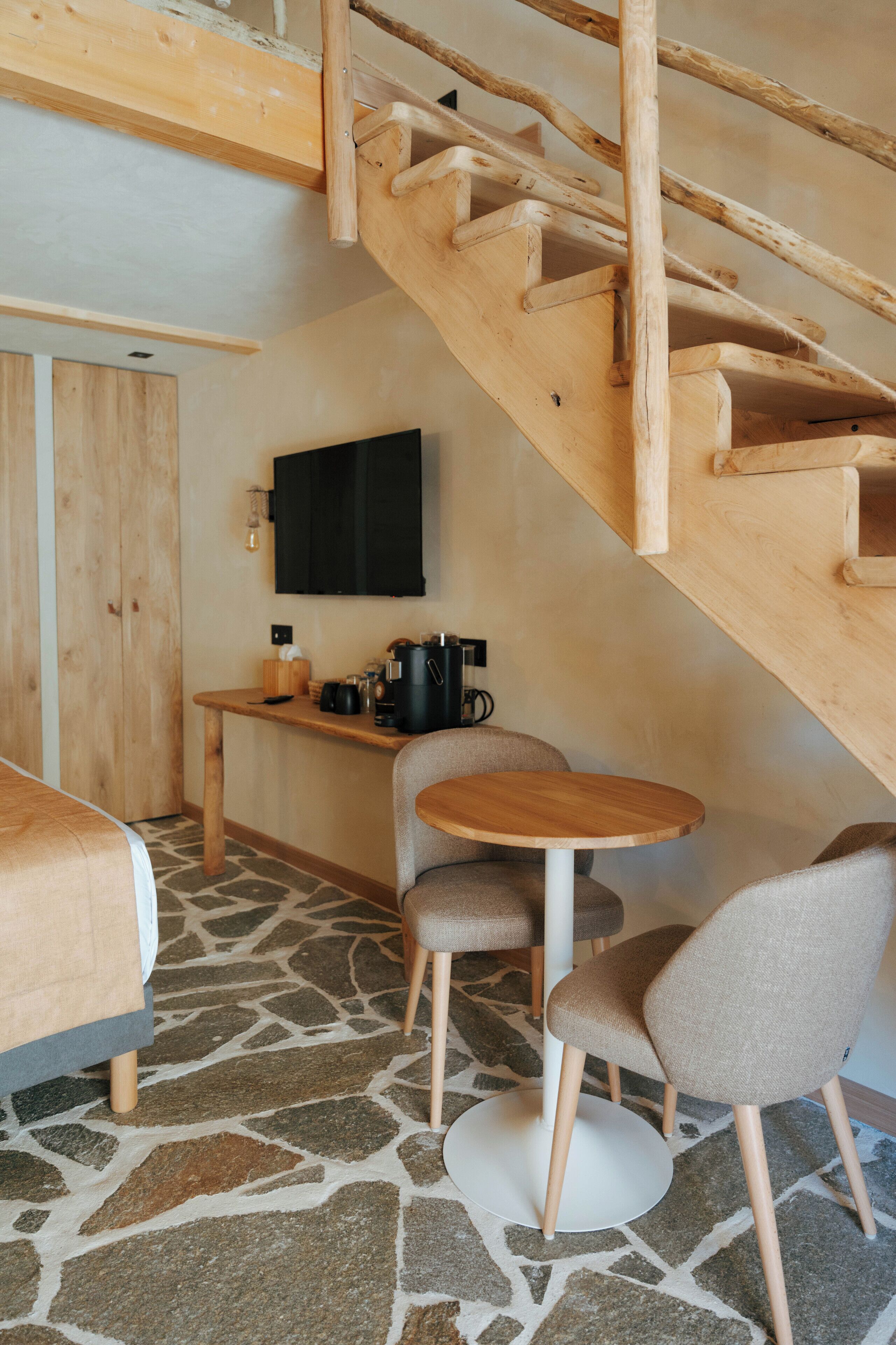 A cozy room with a stone floor, a wooden staircase, a flat-screen TV, a coffee machine, and a small table with chairs.
