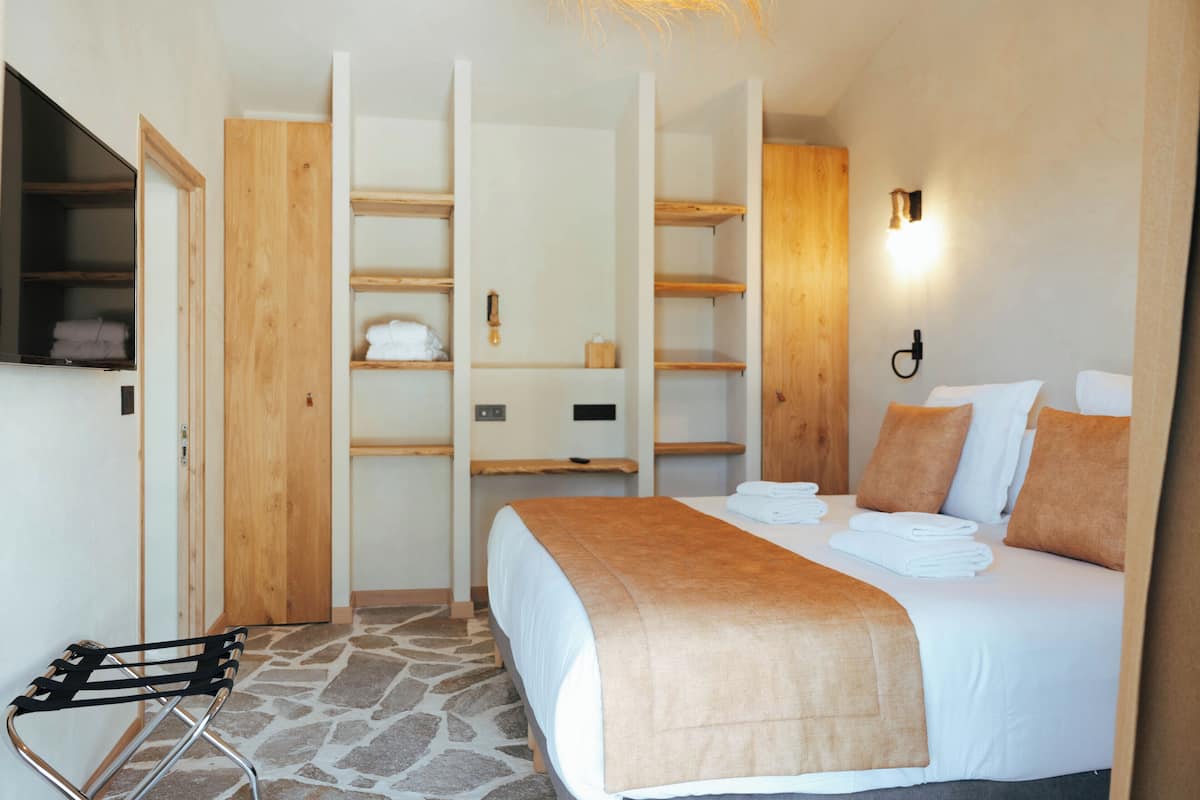 Ein Hotelzimmer mit Bett, Holzschrank, Handtuchhalter und Boden mit Steinmuster.