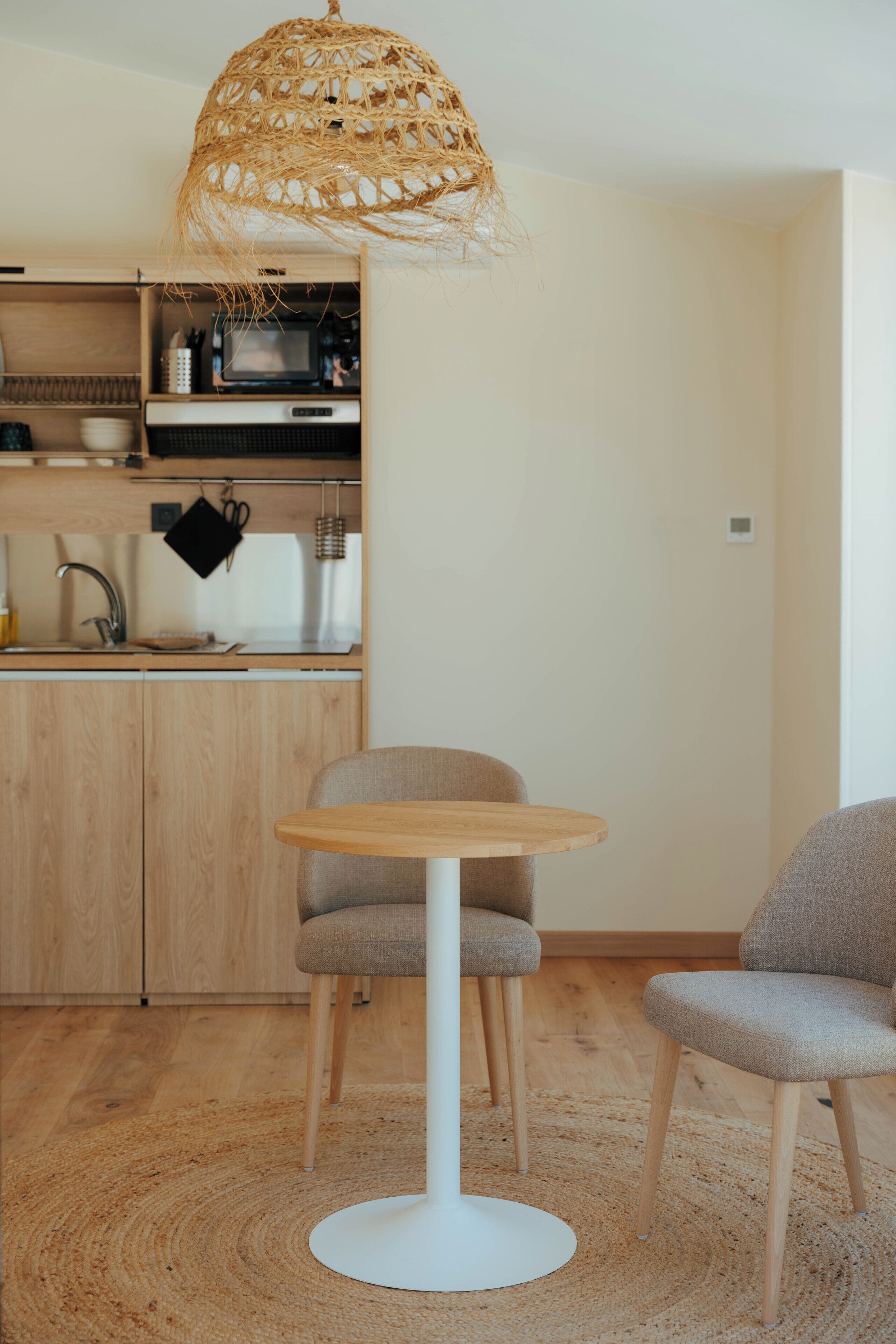 Een moderne keuken met houten kastjes, een ronde witte tafel en twee grijze stoelen.