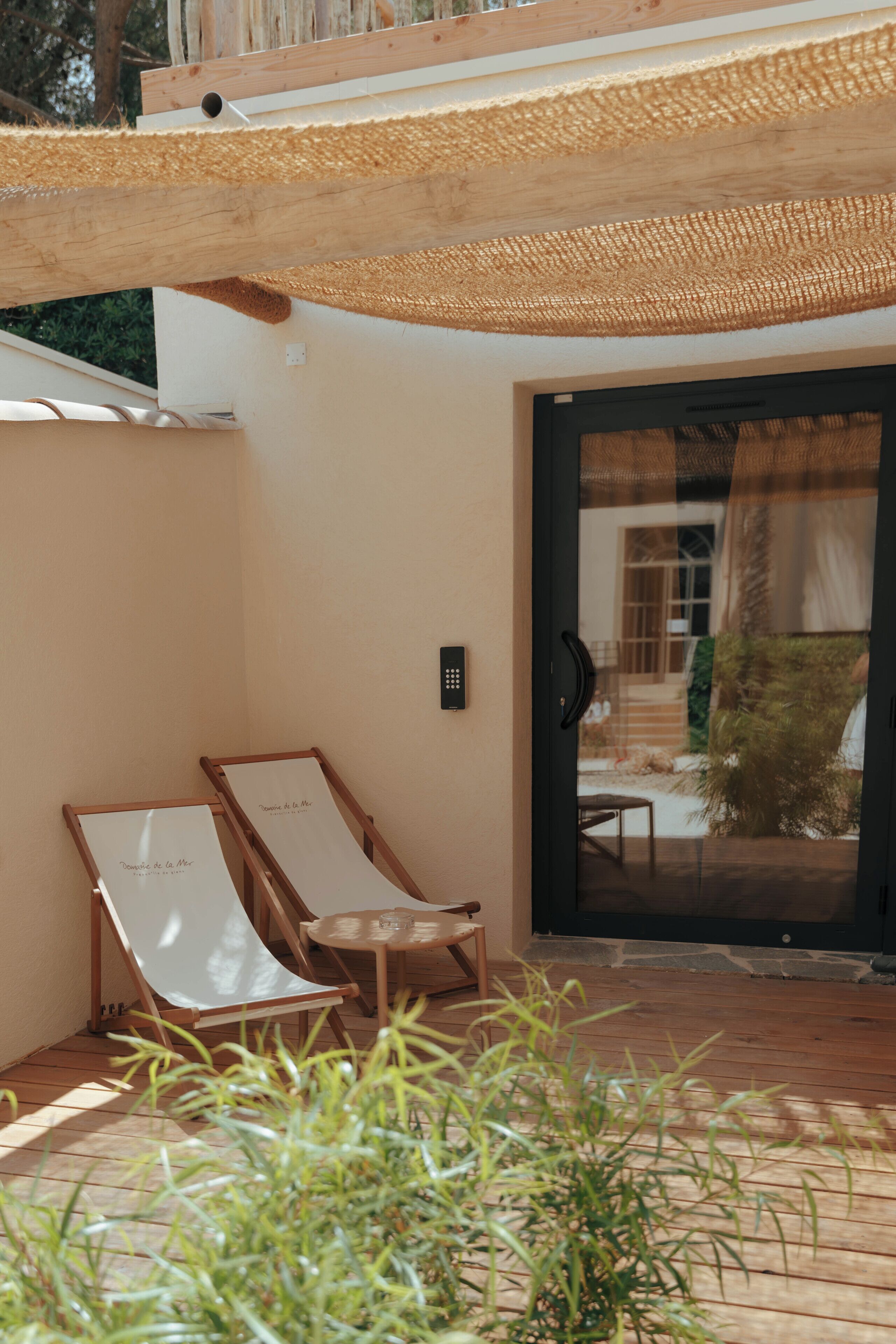 Une terrasse en bois avec deux chaises longues, une petite table et une porte donnant sur un patio abrité.
