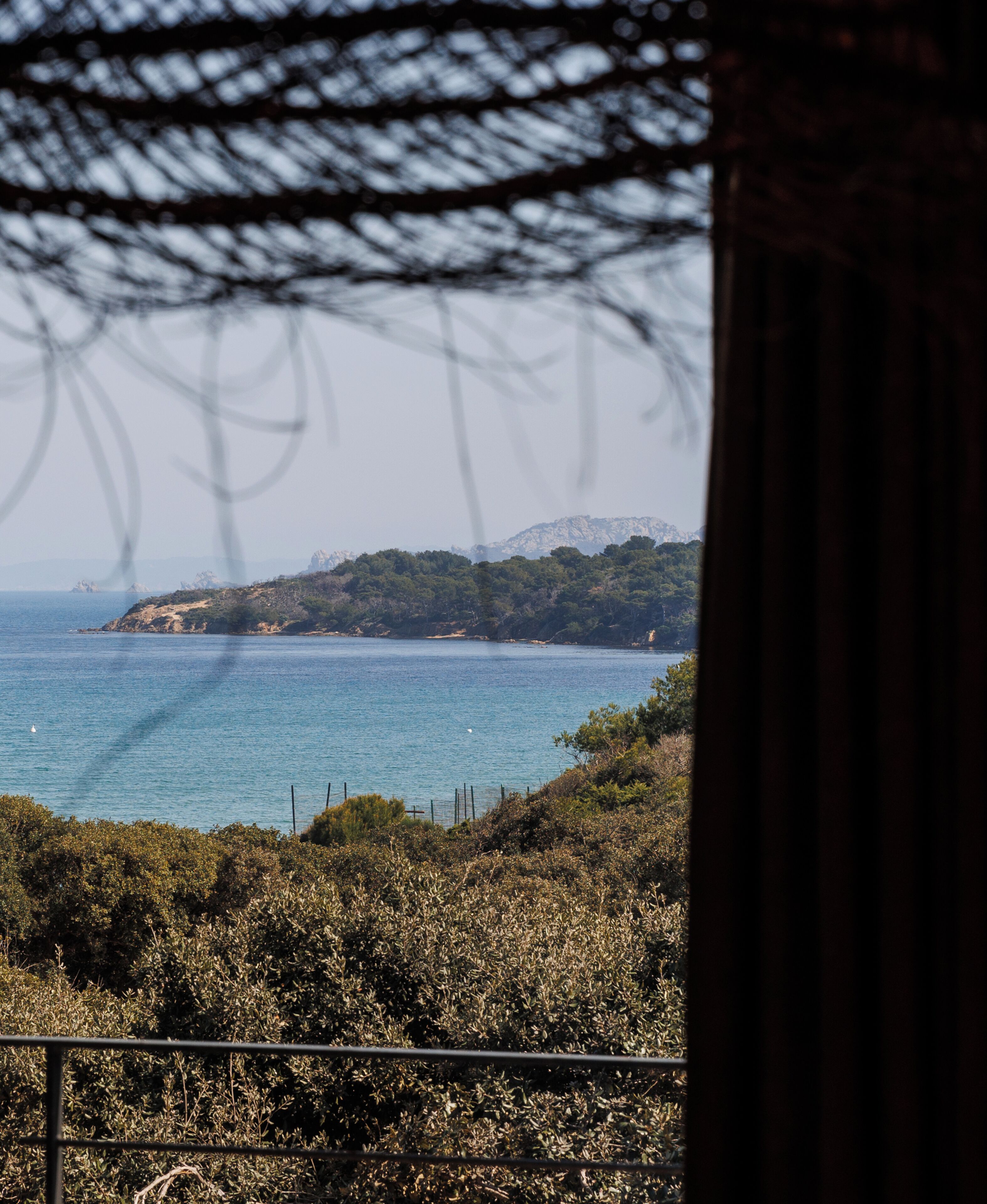 A coastal view with a mountainous backdrop, a body of water, and a fence in the foreground.