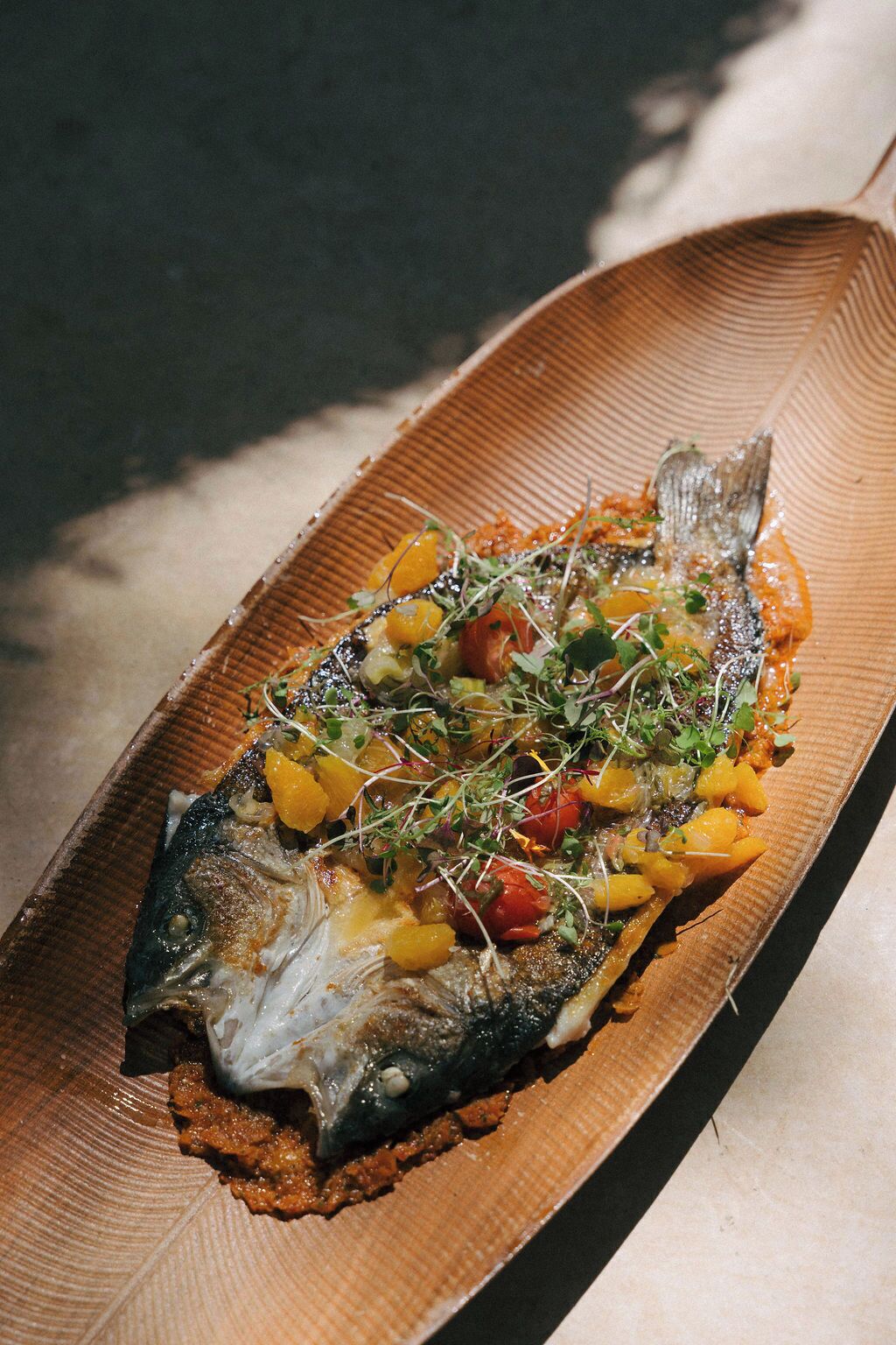 A dish with a fish, vegetables, and sprouts on a wooden plate.