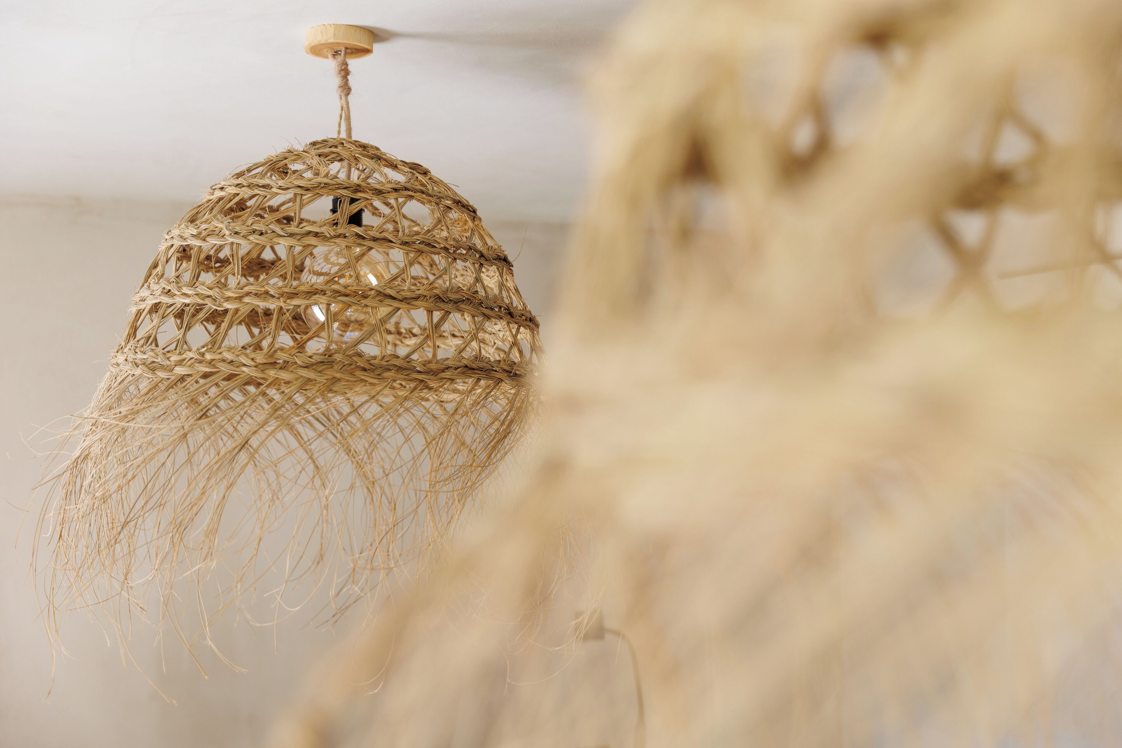 A wicker chandelier with a wooden base and a rope handle.