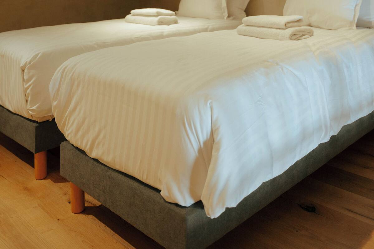 Ein Schlafzimmer mit zwei Betten, jeweils mit weißer Bettwäsche und Kissen, in einem Raum mit schrägem Dach und Einbaustrahlern.