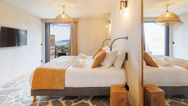 Een tweepersoonsbed met een vloer van steenmotief, een grote spiegel en een balkon met uitzicht.