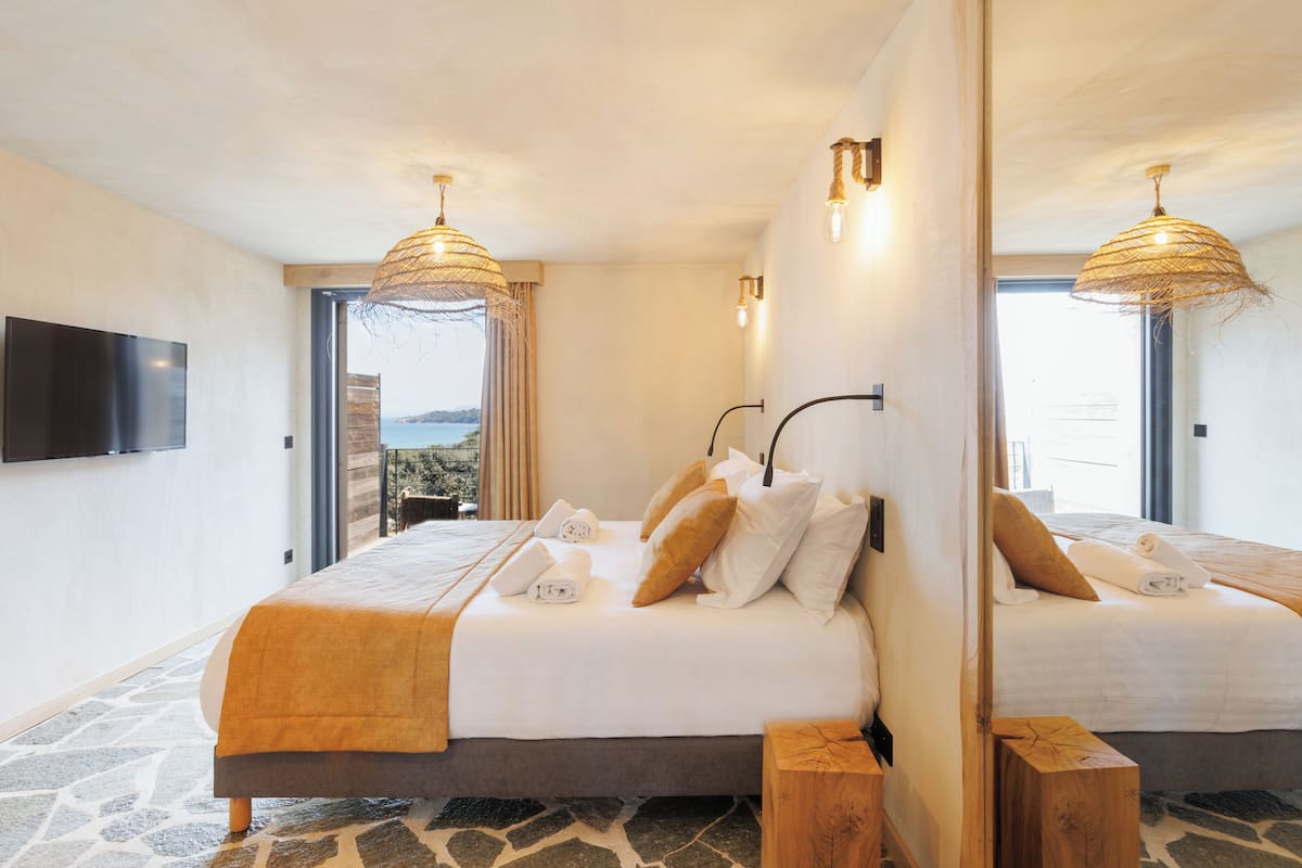 Ein Doppelbett, ein Fußboden mit Steinmuster, ein großer Spiegel und ein Balkon mit Blick.
