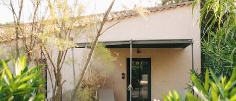 A building with a beige exterior, a covered patio area, and a door with a security camera.