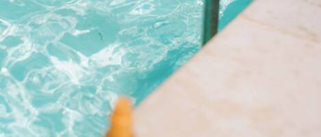 A poolside area with a tiled surface, a bottle, and a book.