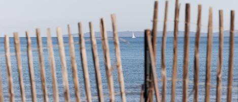 A wooden fence with a view of the sea and a sailboat in the distance.