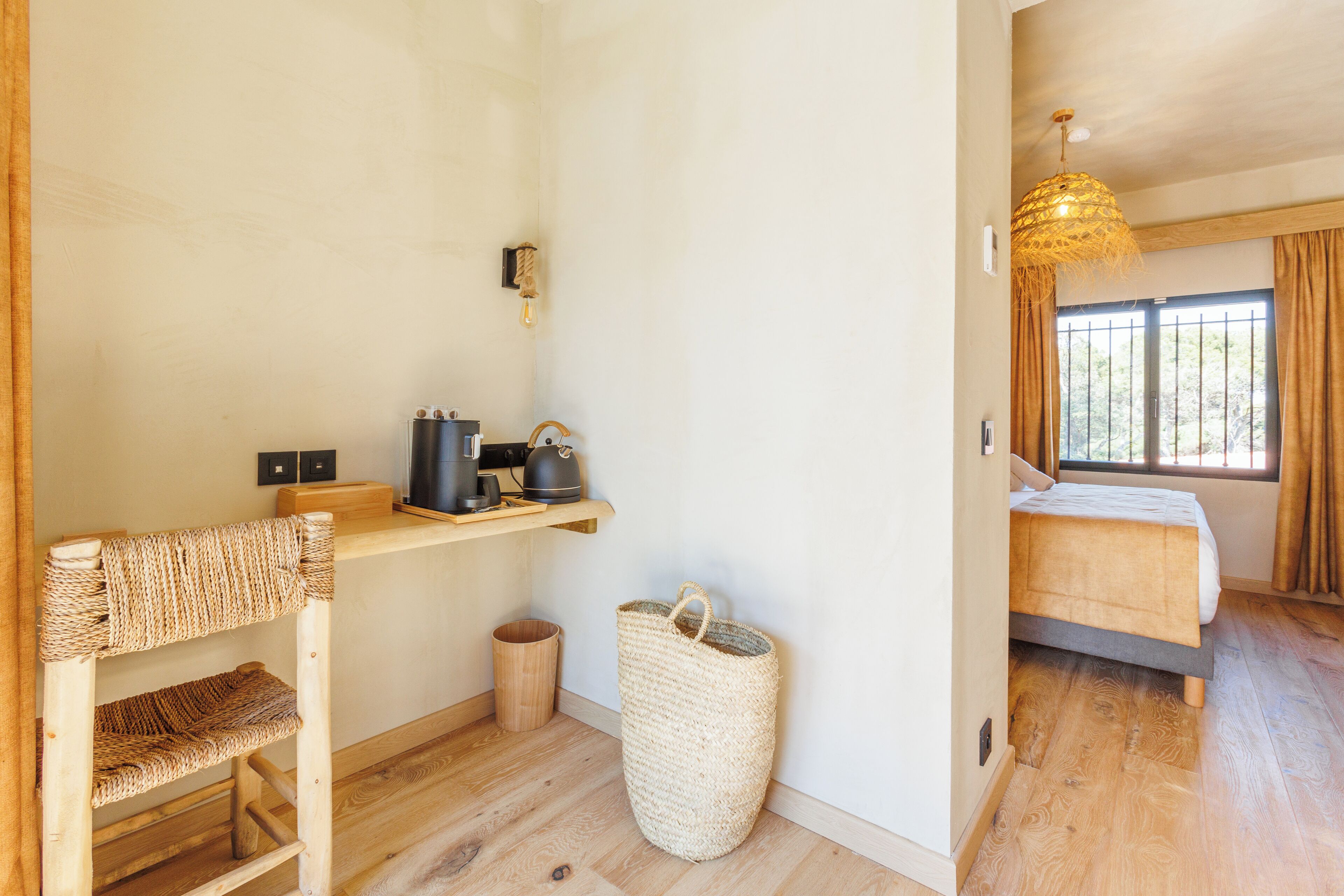 A cozy room with a wooden desk, a bed, a woven basket, and a hanging light fixture.