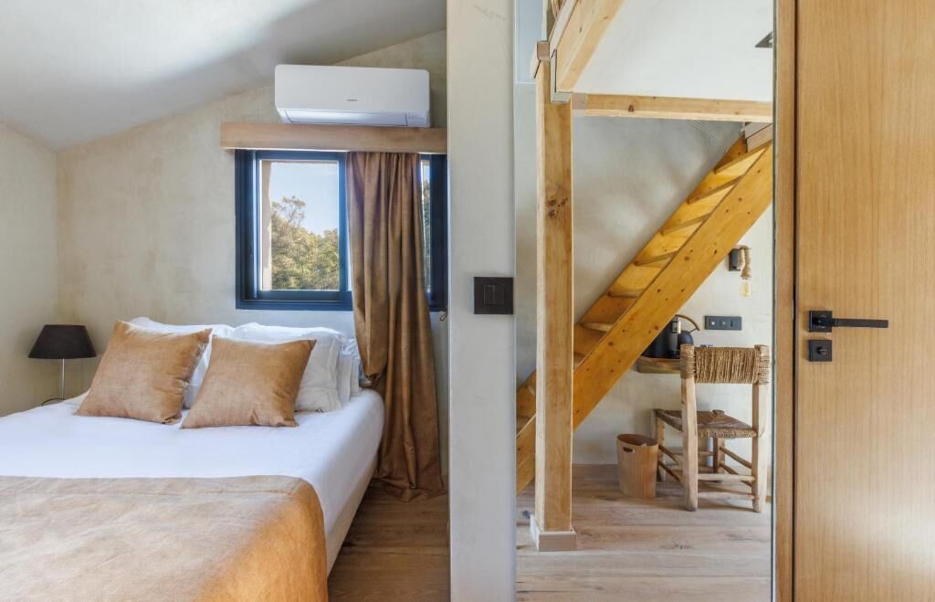 Un dormitorio con cama, ventana con cortinas, equipo de aire acondicionado y una escalera de madera que conduce a un nivel superior.