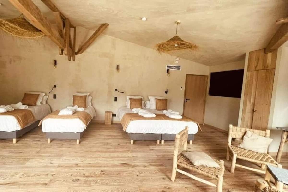 Ein rustikales Schlafzimmer mit drei Holzbetten, einem gewebten Sessel und einem Holztisch.