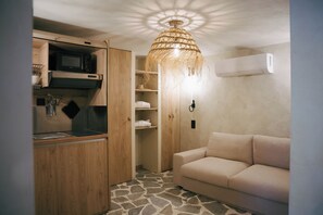 Un ambiente compatto con angolo cottura, lampada in fibra naturale, divano color beige e pavimento effetto pietra.