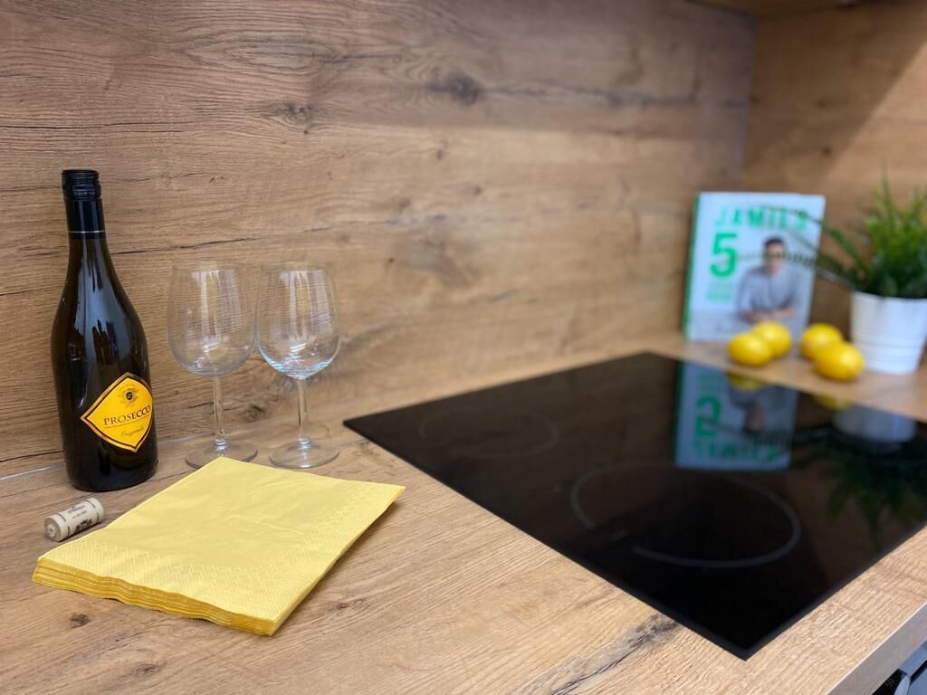 Une table en bois sur laquelle se trouvent une bouteille de vin, deux verres, une serviette jaune, une petite carte et des citrons.