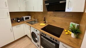A compact kitchen with white cabinets, a microwave, a sink, a stove, and a washing machine. - Stylische Wohnung mit Traumausblick in Dornbirn (Dornbirn)