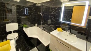 A modern bathroom with a black marble backsplash, a white bathtub, a vanity with a mirror, and a toilet. - Stylische Wohnung mit Traumausblick in Dornbirn (Dornbirn)