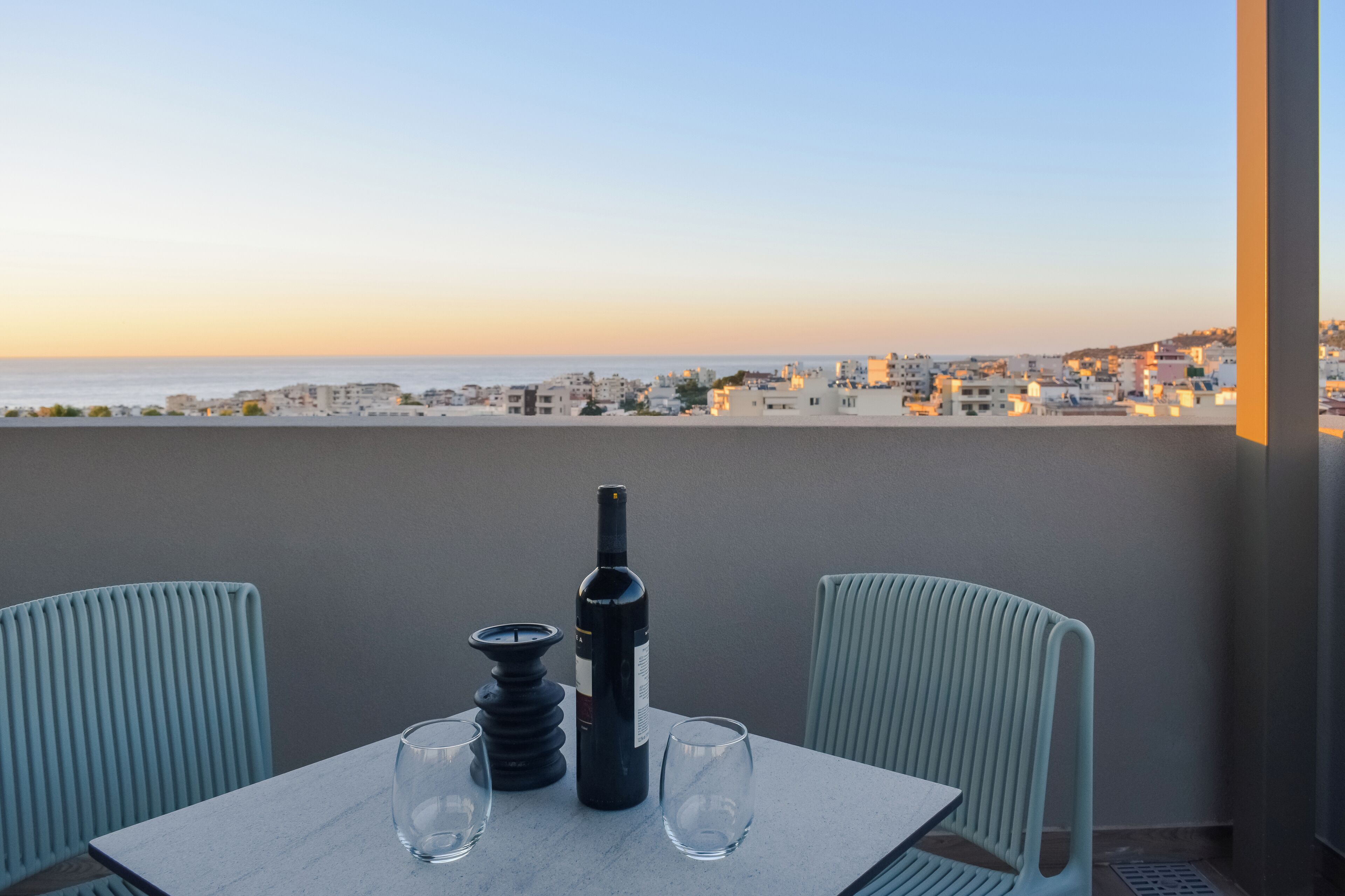 Une table avec une bouteille et des verres sur un balcon donnant sur une vue panoramique de la ville.