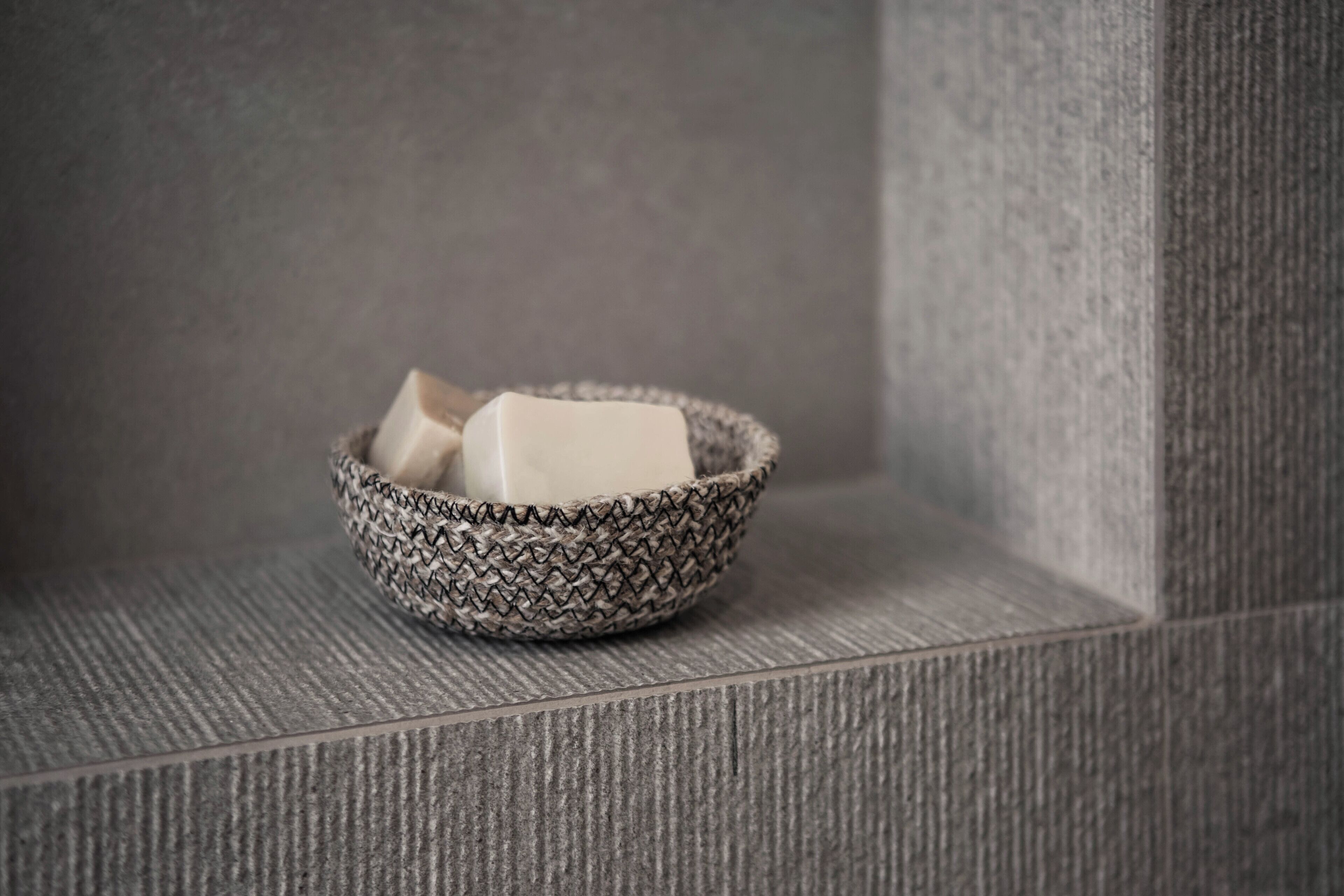 A woven basket containing a bar of soap on a textured grey surface.