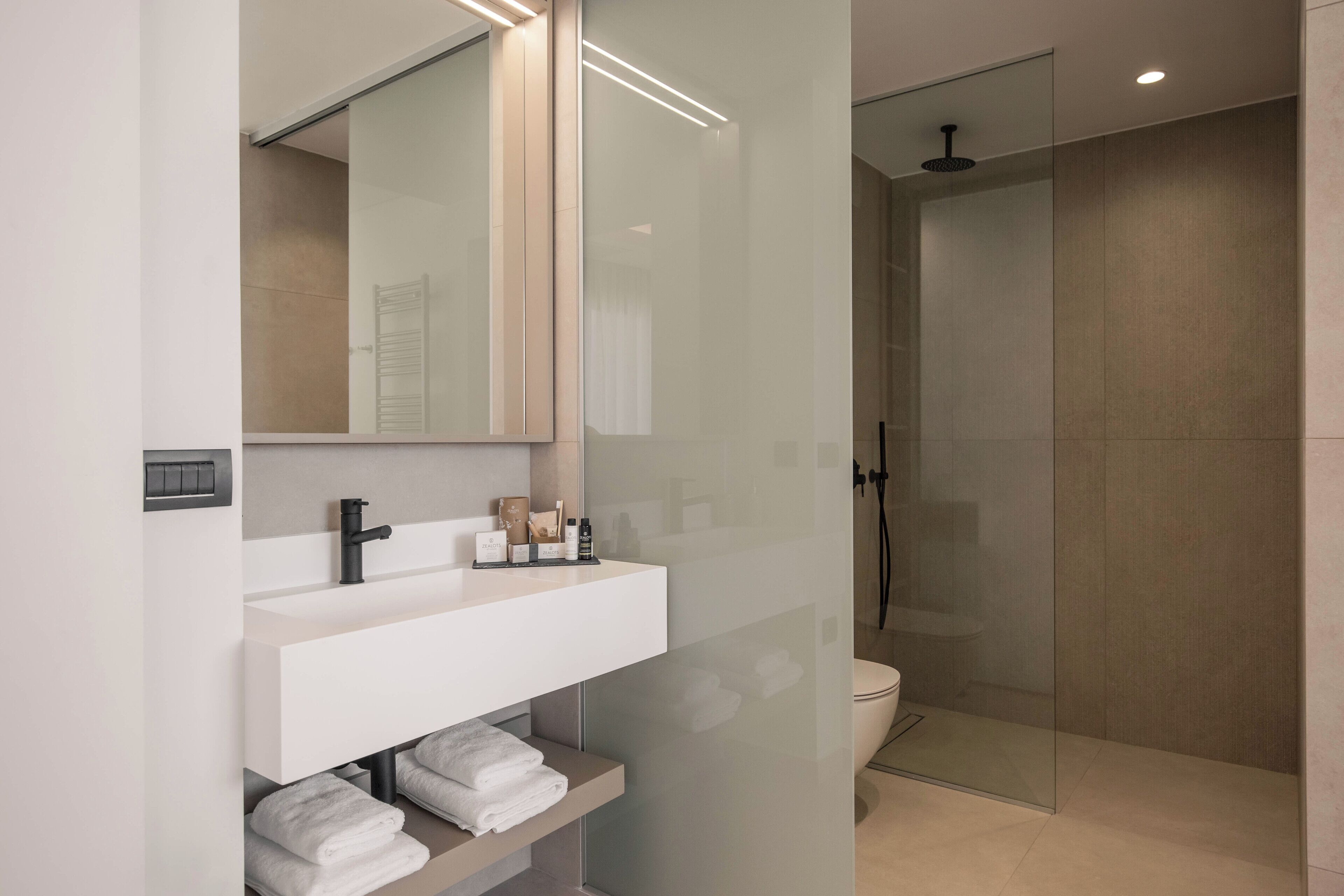 Une salle de bain moderne avec une douche à parois de verre, un meuble-lavabo blanc avec un miroir et des serviettes soigneusement pliées sur une étagère.
