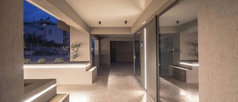 A modern hallway with a glass door leading to a kitchen area, a built-in bench, and a view of the outside at dusk.
