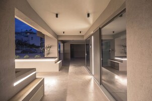 Ένας σύγχρονος διάδρομος με μια γυάλινη πόρτα που οδηγεί σε μια κουζίνα, έναν εντοιχισμένο πάγκο και θέα προς τα έξω κατά τη διάρκεια του λυκόφωτος.