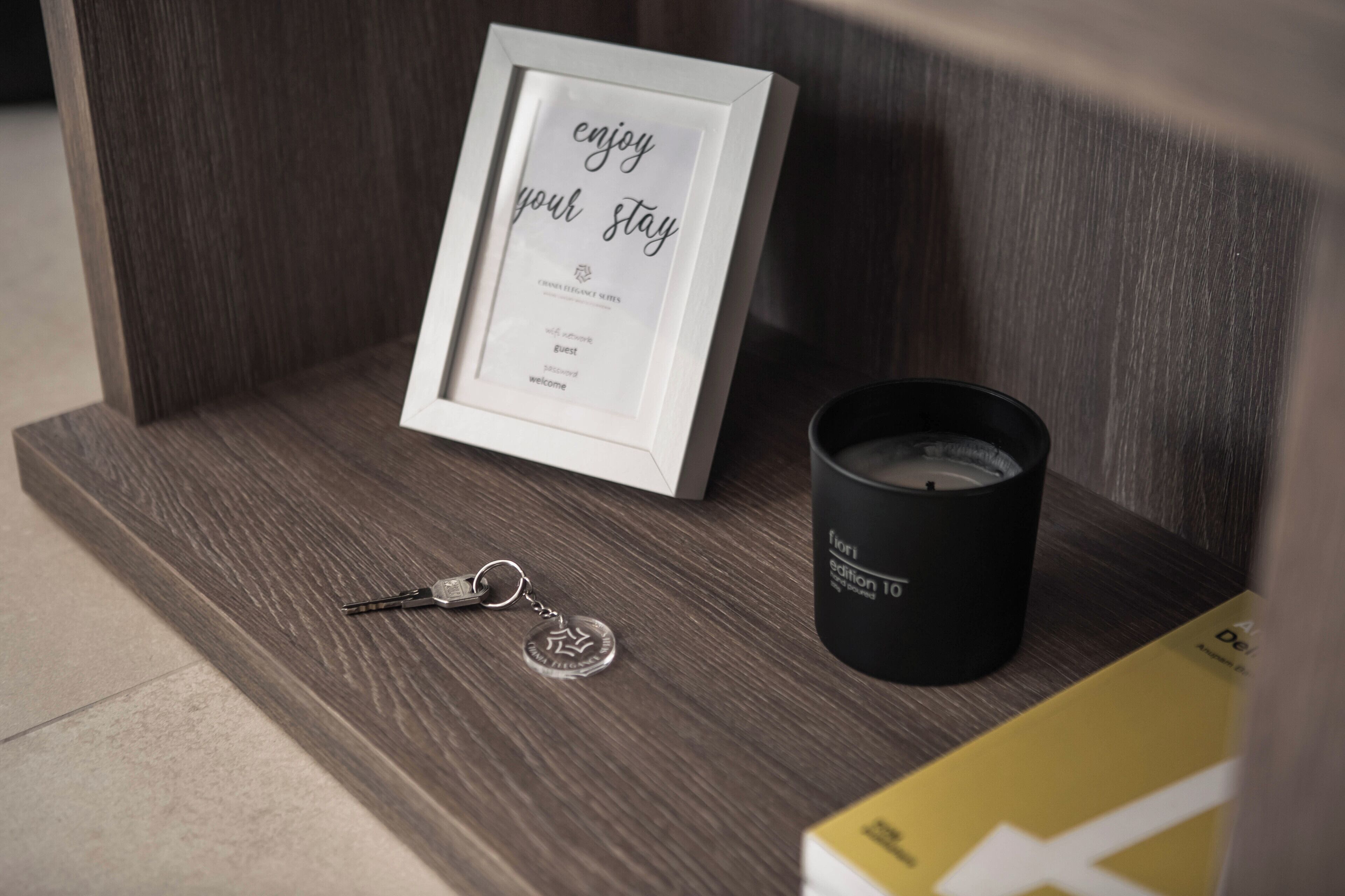 A framed sign with the text "enjoy your stay," a black candle, and a keychain on a wooden shelf.
