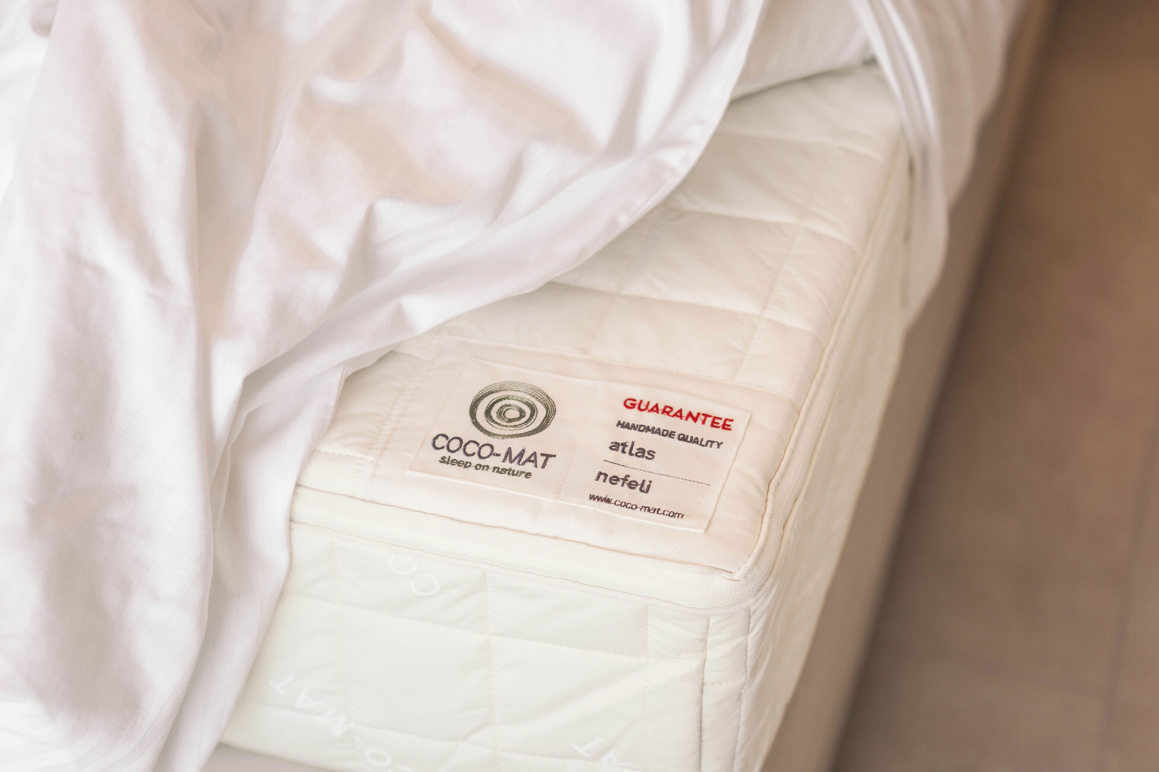 A white mattress with a label indicating it is a COCO-MAT atlas sleep on nature product.