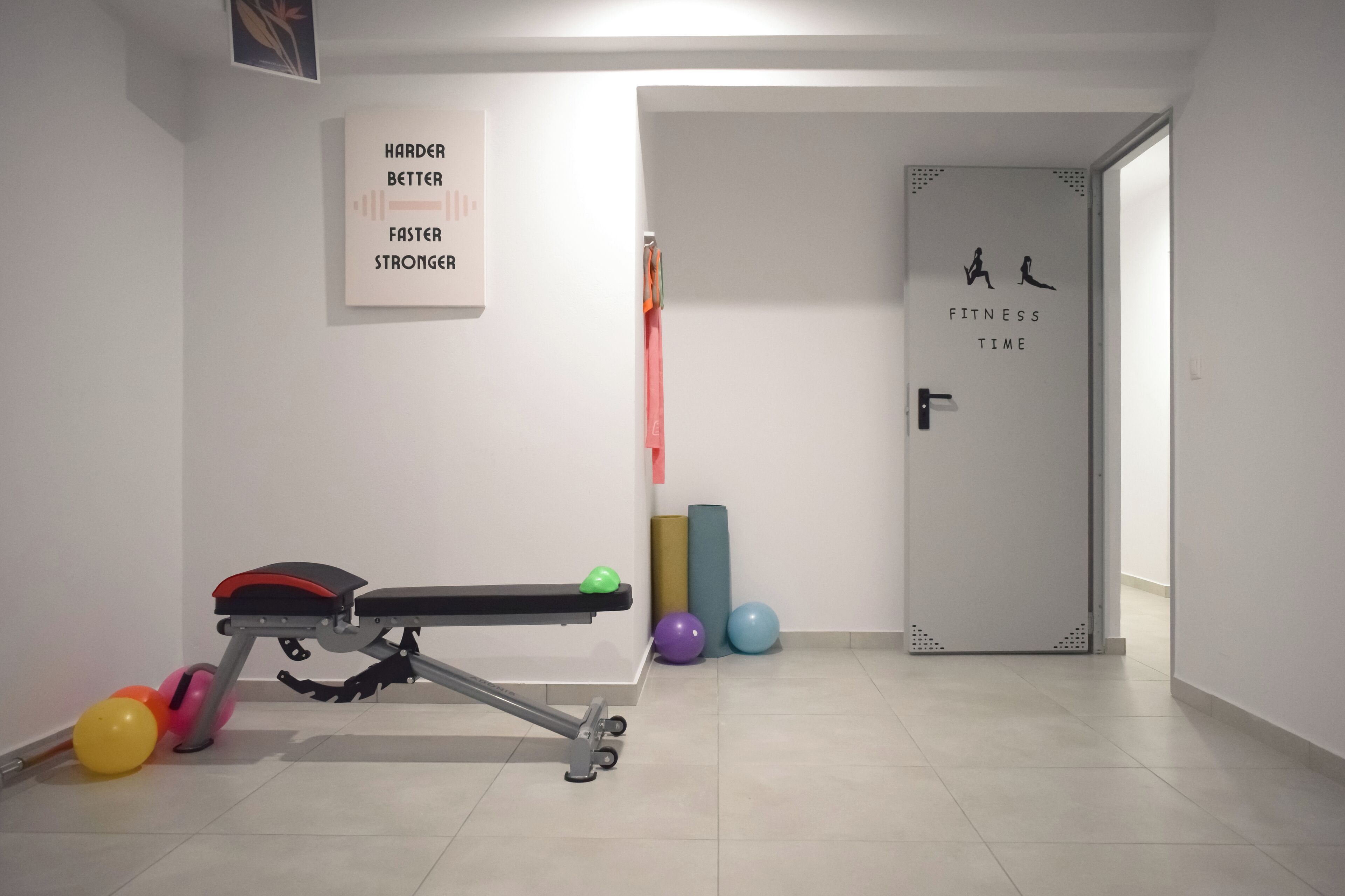 Un gimnasio con equipo de ejercicio, un cartel motivacional y una puerta que dice "FITNESS TIME".