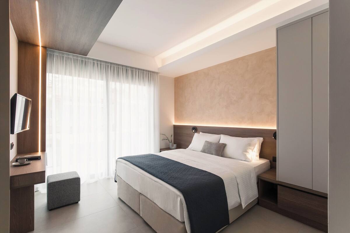 A modern hotel room with a large bed, bedside tables, a TV, and a wardrobe.
