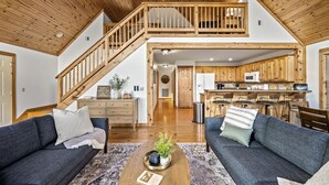 Un vaste salon doté d’un haut plafond, d’un escalier en bois et d’un coin cuisine avec des meubles en bois et un four à micro-ondes.