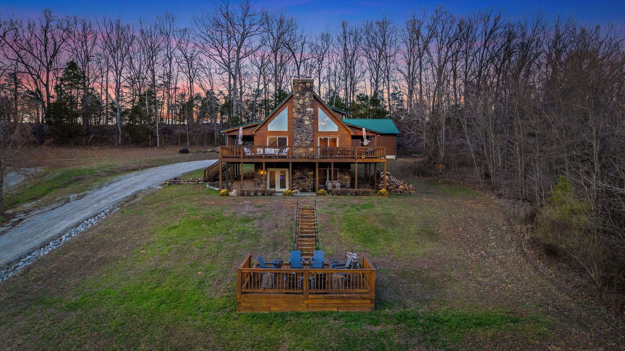 A large wooden cabin with a stone chimney, a porch with outdoor seating, and a view of the surrounding forest.