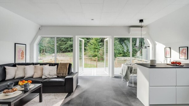 Ein modernes Interieur mit Sofa, Esstisch und Küchenbereich, ausgestattet mit großen Fenstern und Blick auf Grünflächen.