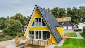 Ein zweistöckiges gelbes Haus mit einem Balkon, einer Holzterrasse und einer Schotterauffahrt.