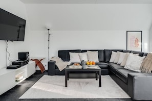 Un salon moderne avec un canapé en cuir noir, une table basse et un téléviseur à écran plat fixé au mur.