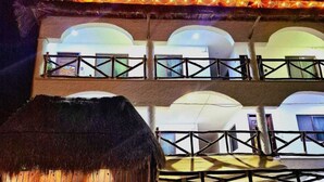 A multi-story building with a thatched-roof structure at the entrance, balconies with railings, and a series of windows on each floor. - Hotel Villas Ponto Holbox (Isla Holbox)