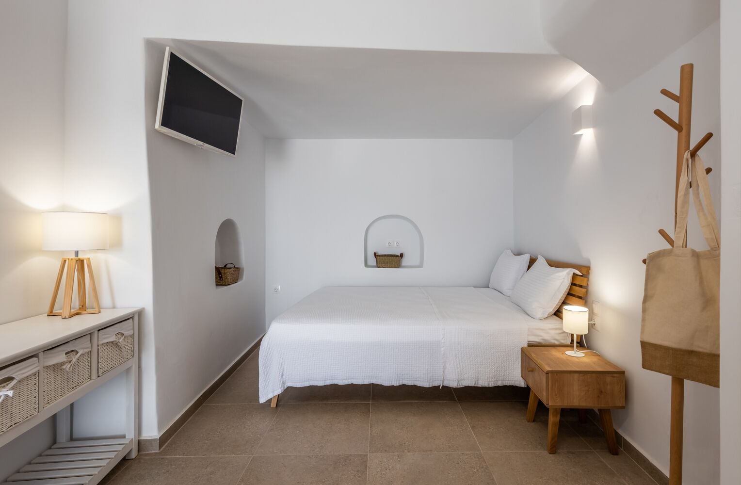 Un dormitorio con cama, mesitas de noche, televisión y perchero.