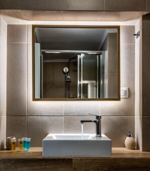 A modern bathroom with a rectangular sink, a glass-enclosed shower, and a large mirror above the sink. - Anemi Suites (Milos)