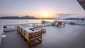 A rooftop terrace with wooden furniture and a view of the sunset over the water. - Anemi Suites (Milos)