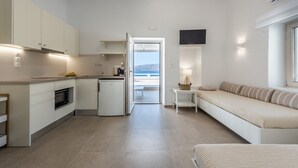 A compact, modern kitchen with integrated appliances, a dining area with a bench, and a view of the sea through an open door. - Anemi Suites (Milos)