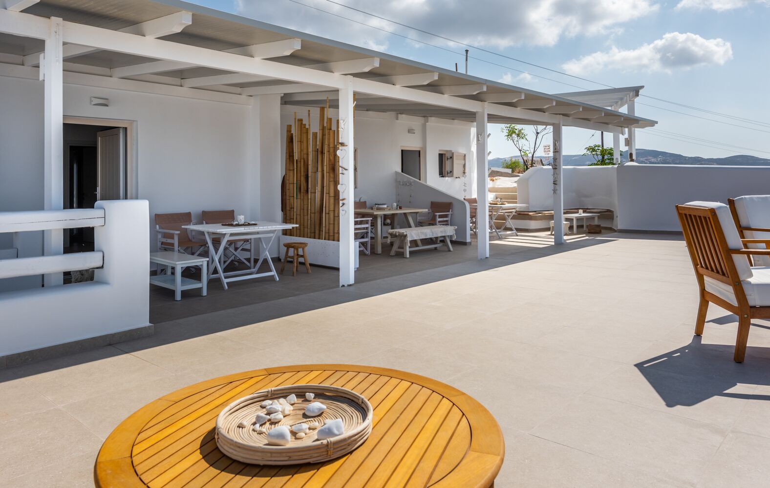An outdoor patio area with white furniture, a round wooden table with stones, and a view of the landscape.