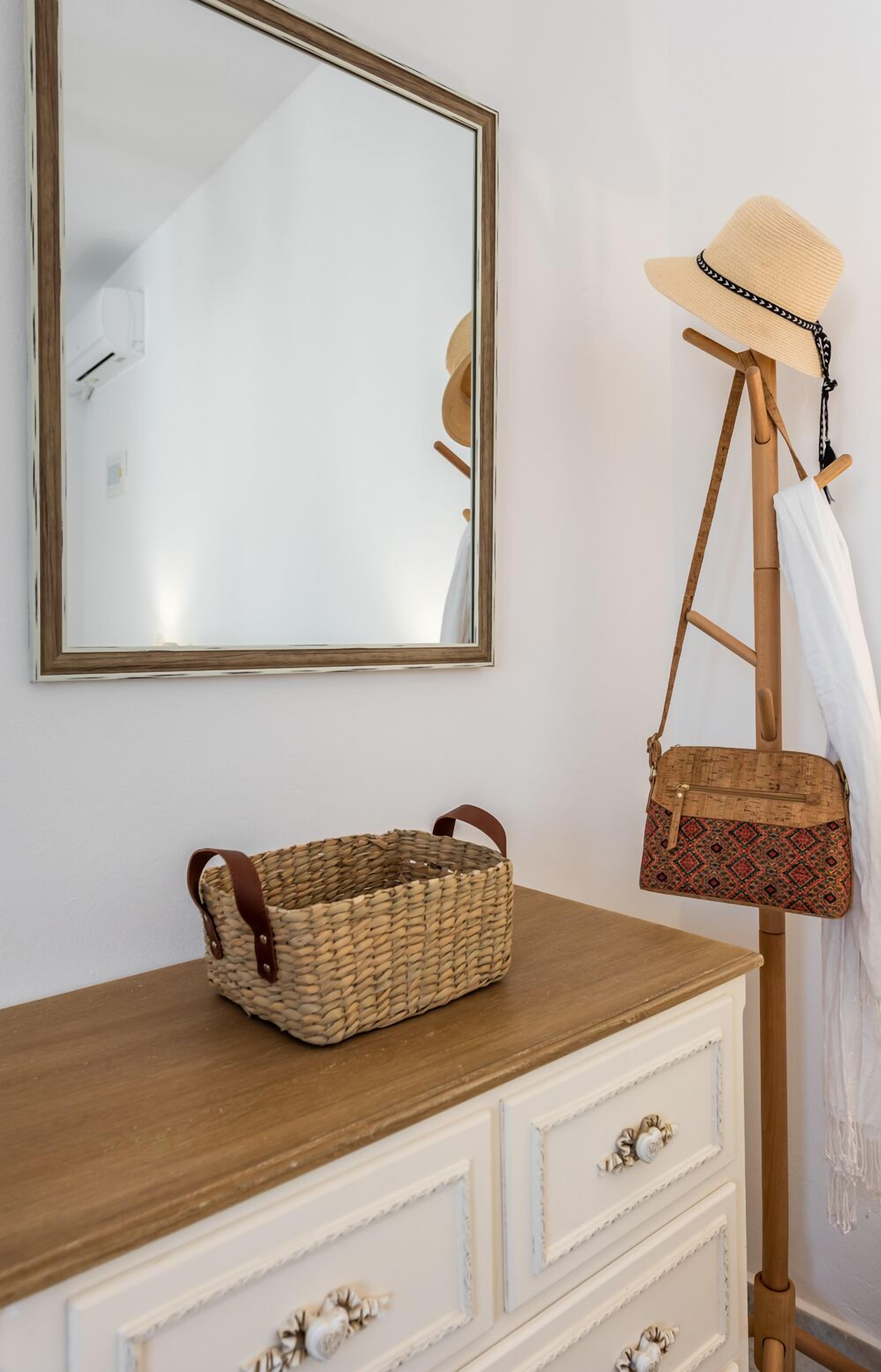 Un aparador de madera con cajones, una cesta tejida, un bolso de corcho y un sombrero de paja sobre un soporte de madera.