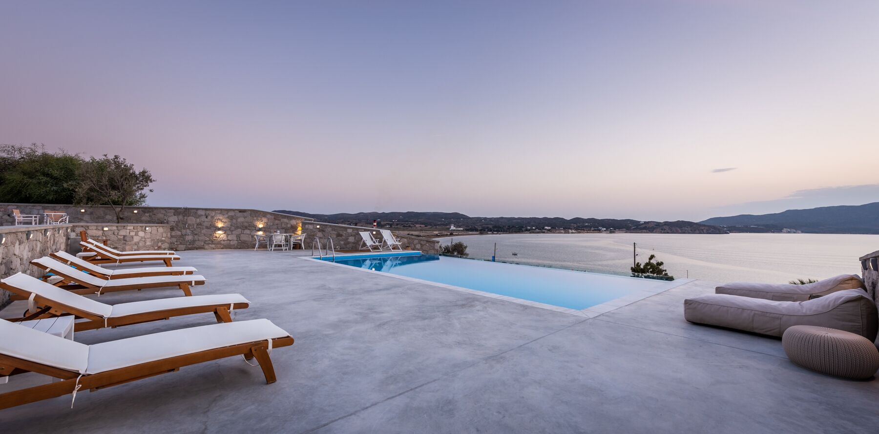 Zona de piscina en la azotea con sillones de descanso y una piscina pequeña, con vistas a una masa de agua y colinas lejanas.